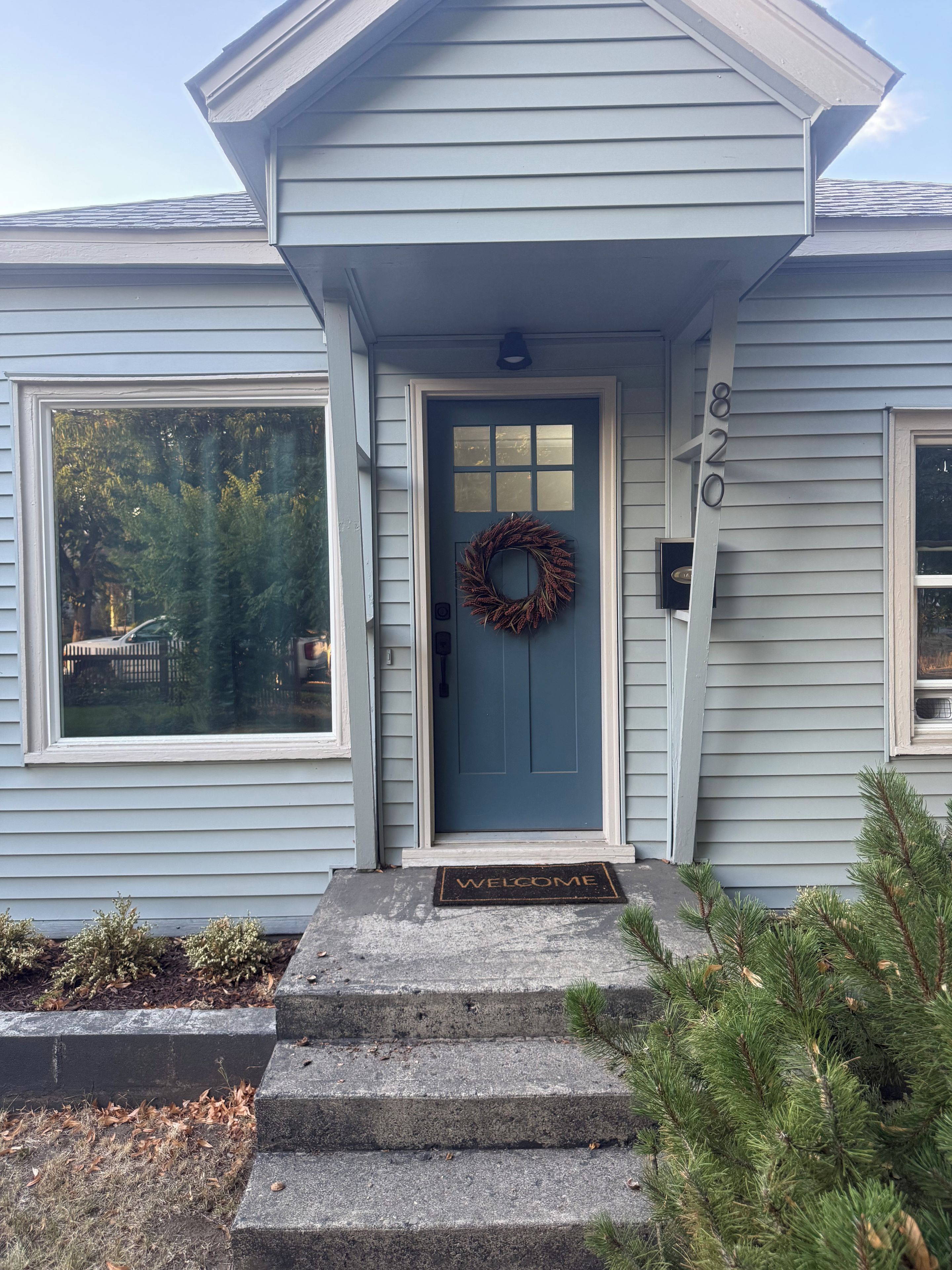 A house with a blue front door, a welcome mat, and a number '820' on the wall.