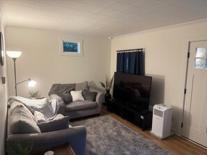Una sala de estar con un sofá, un televisor, una lámpara de pie y un aire acondicionado instalado en la pared.
