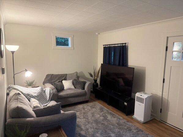 A living room with a sofa, a television, a floor lamp, and a wall-mounted air conditioner. - Bennett Burrow! Newly Renovated home 8 Blocks from Spokane Arena/Riverfront Park (Spokane)