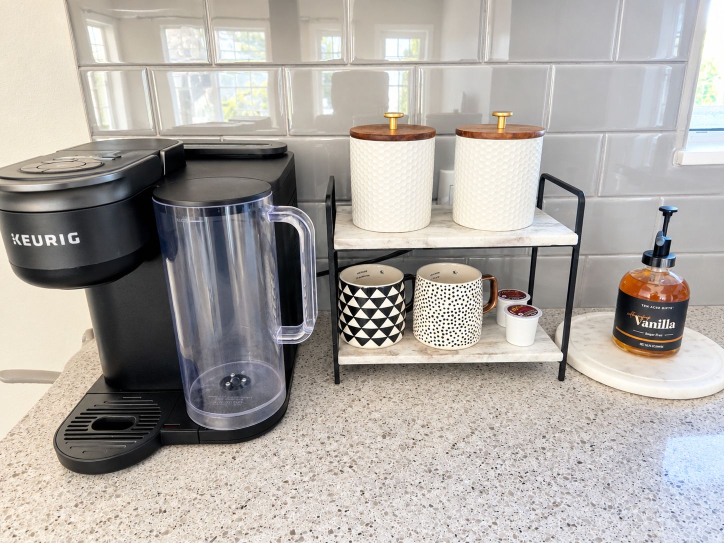 A kitchen with a Keurig coffee maker, a clear mug, two wooden tumblers, patterned mugs, a soap dispenser, and a marble countertop.