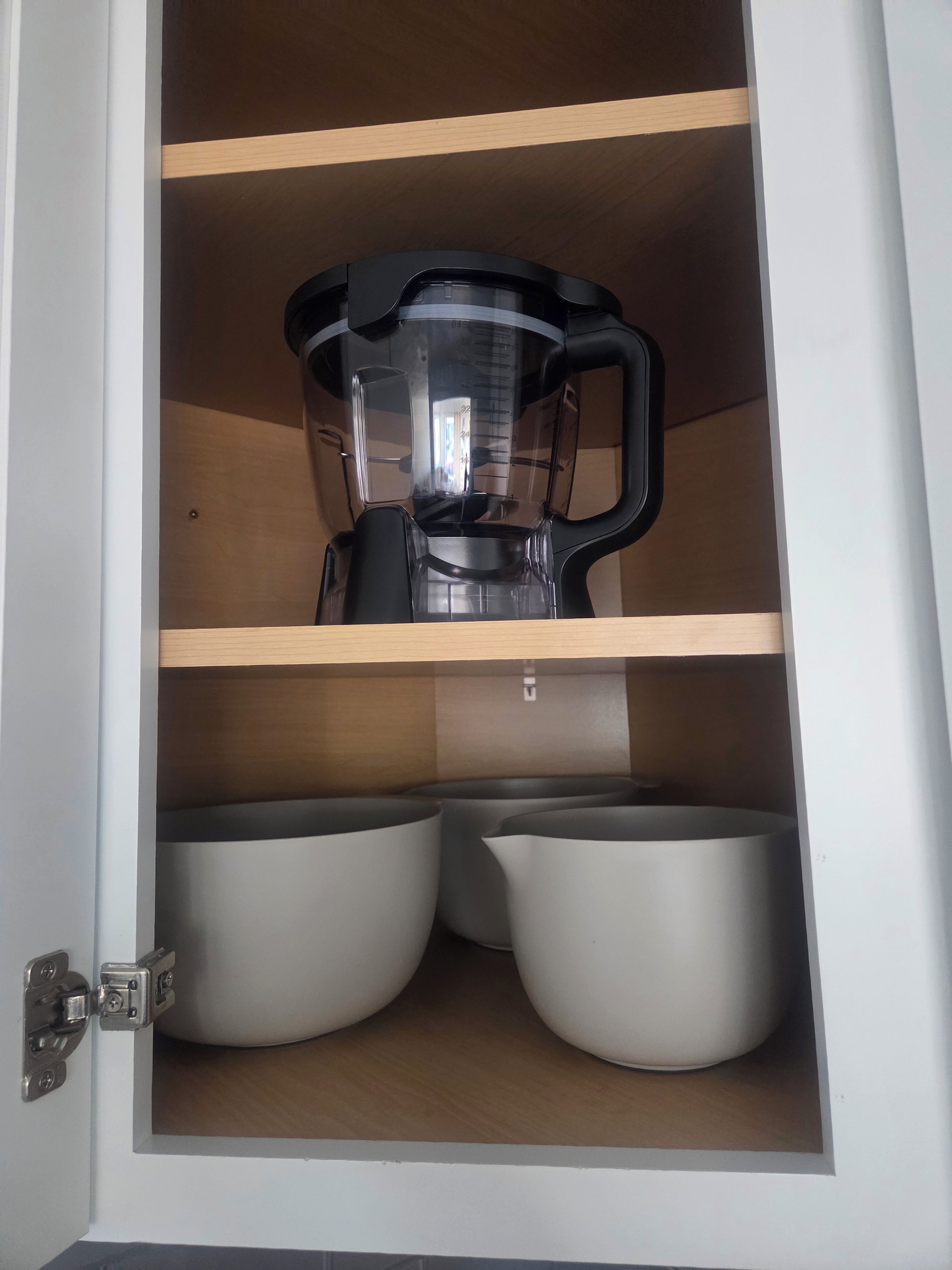 A kitchen cabinet with a blender on the top shelf and two bowls on the bottom shelf.