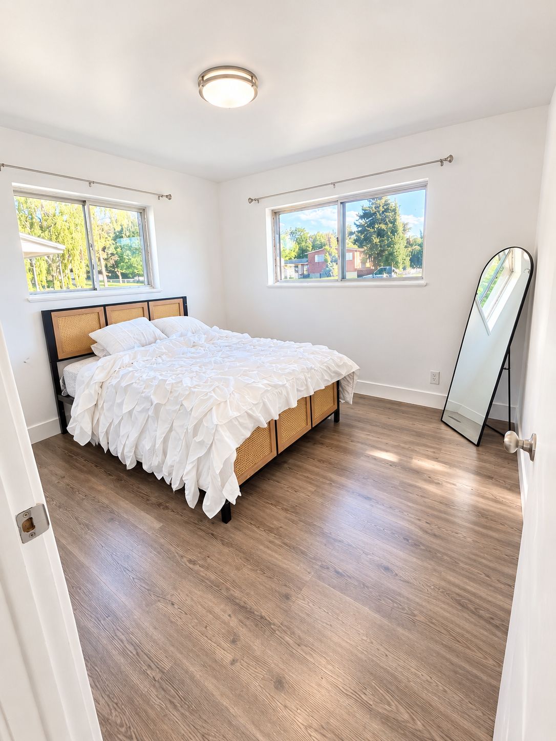 Un dormitorio con cama, suelo de madera y dos ventanas con cortinas.