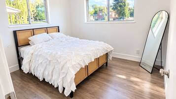 Un dormitorio con cama, suelo de madera y dos ventanas con cortinas.