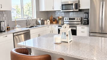 Una cocina moderna con armarios blancos, electrodomésticos de acero inoxidable, encimera de granito y dos taburetes de cuero.