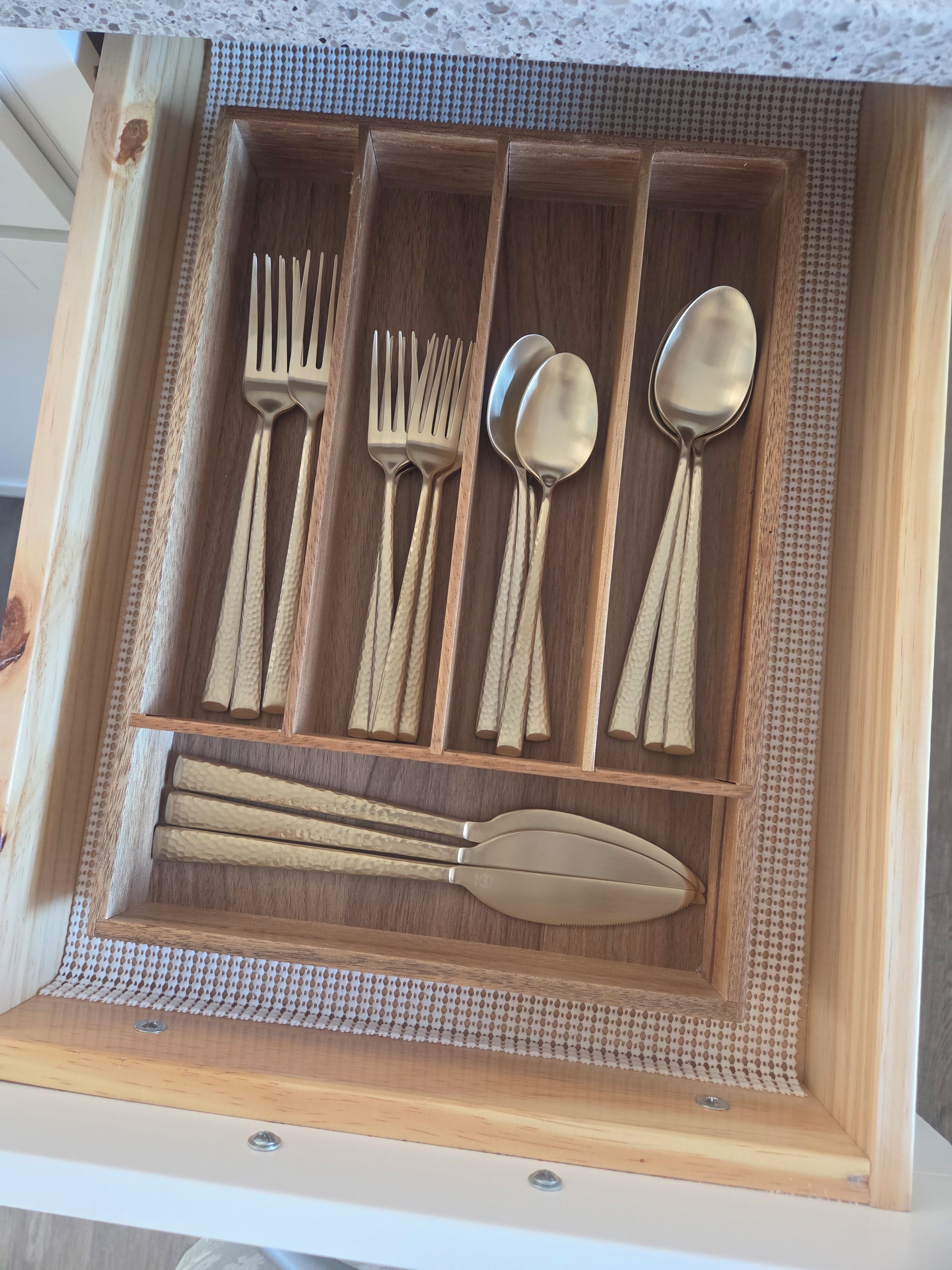 A drawer with a wooden interior containing a set of utensils including forks, spoons, and a knife.