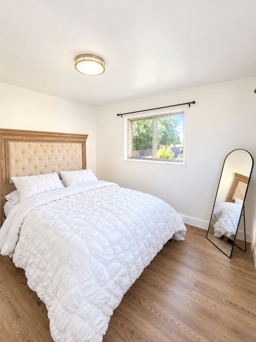 Un dormitorio con una cama grande, una ventana con vistas, una lámpara de techo y un espejo.