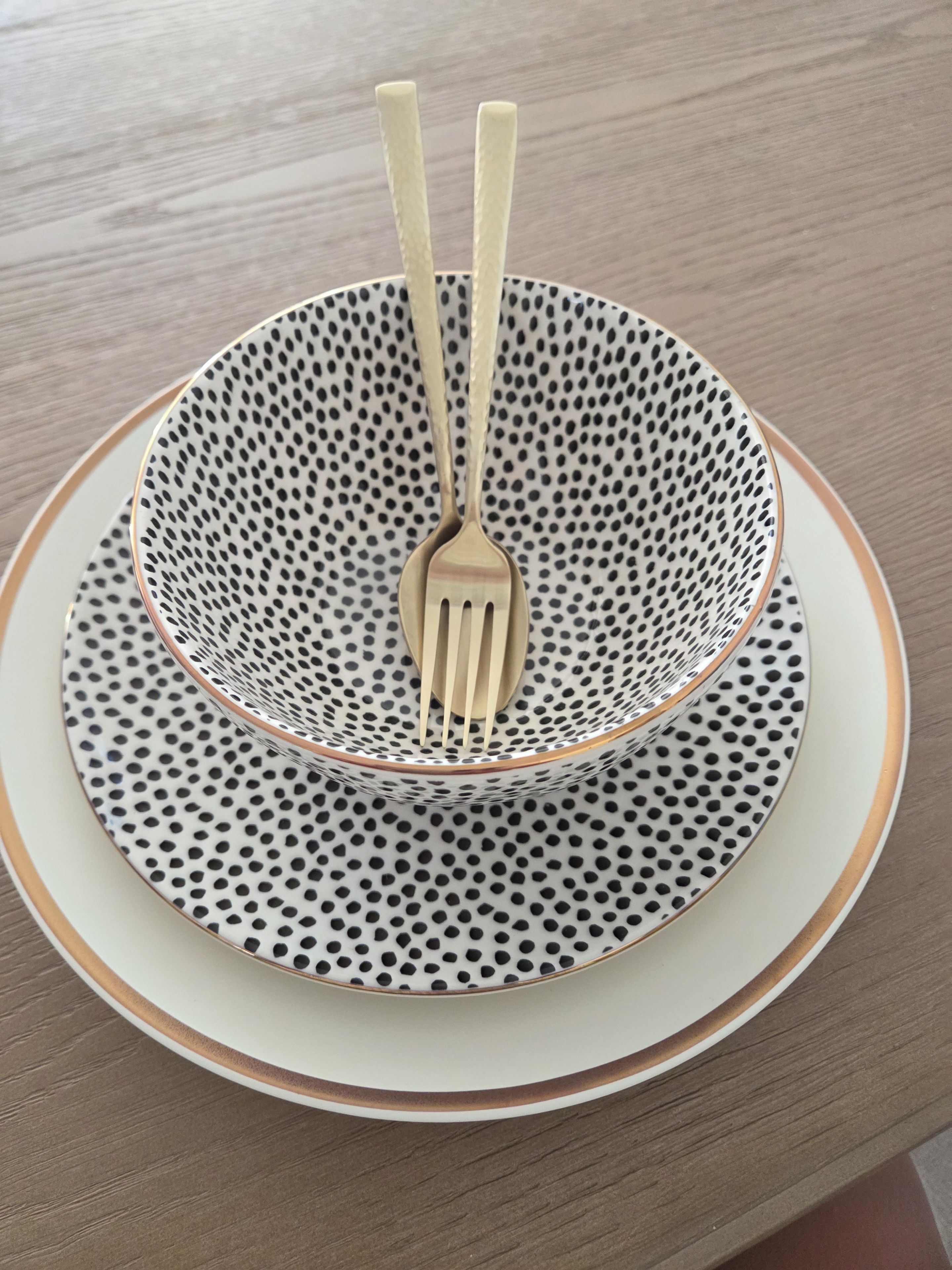 Una mesa puesta con un plato blanco, un cuenco blanco y negro estampado y un tenedor.