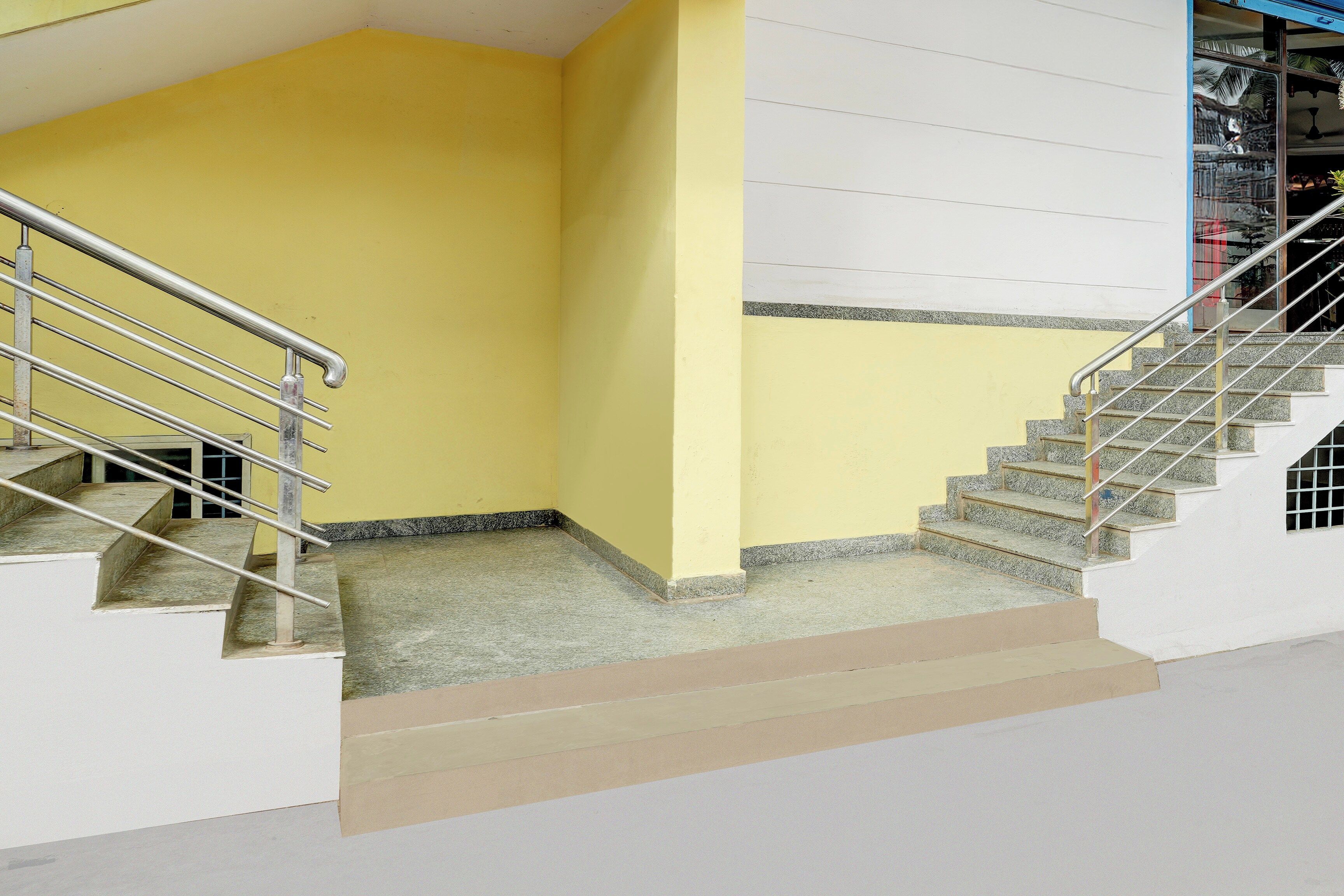 Una escalera con barandillas de metal que lleva a una plataforma con una pared blanca y una pared amarilla.
