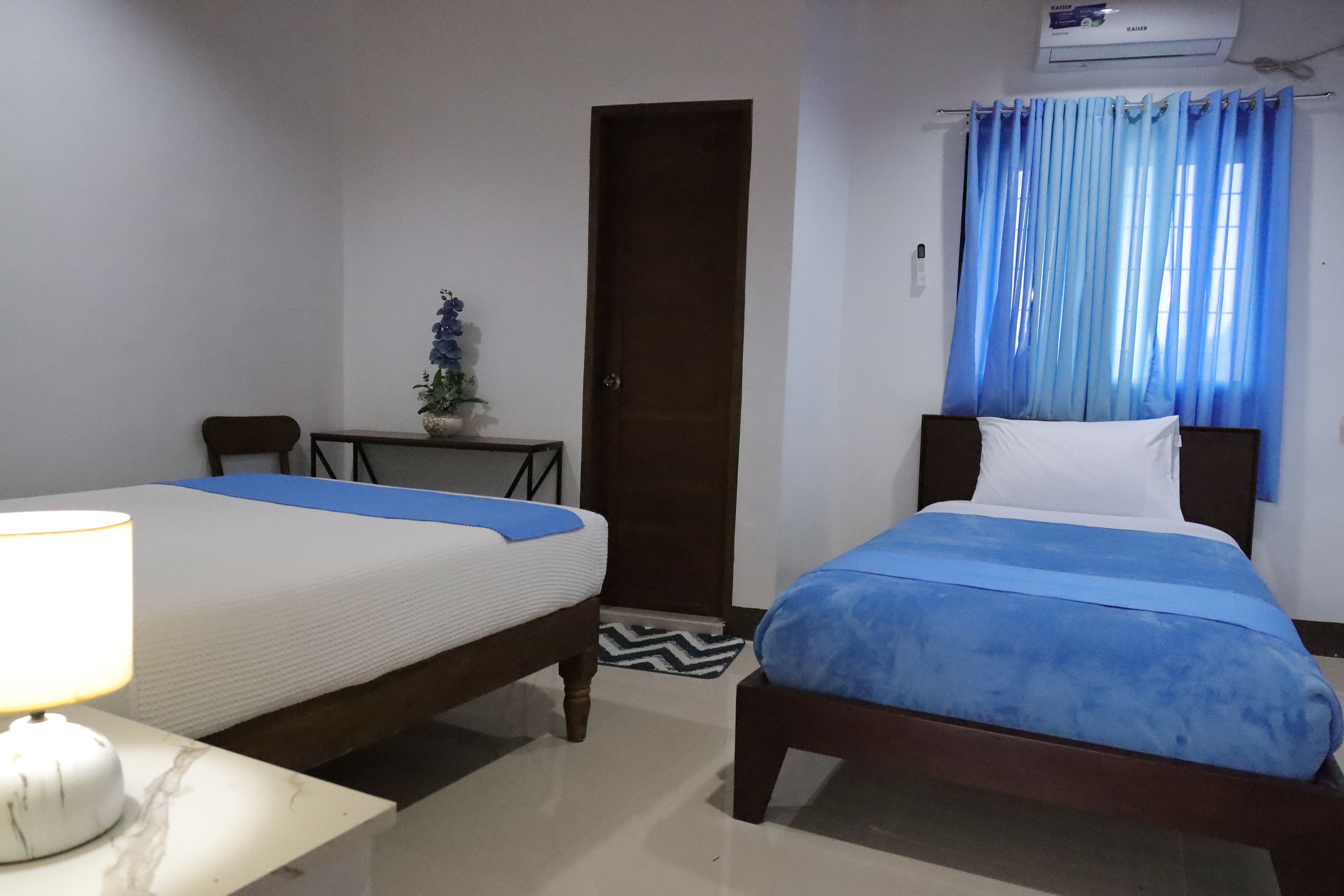 Habitación de hotel con dos camas, un escritorio, una silla, una planta en maceta y una ventana con cortinas.