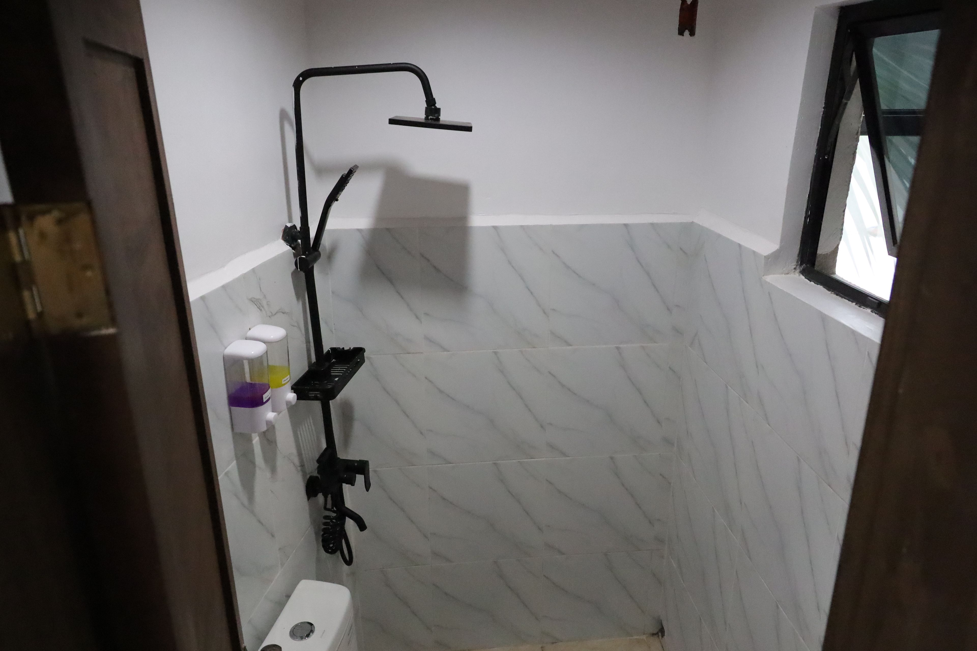 A bathroom with a shower, a toilet, and a window.