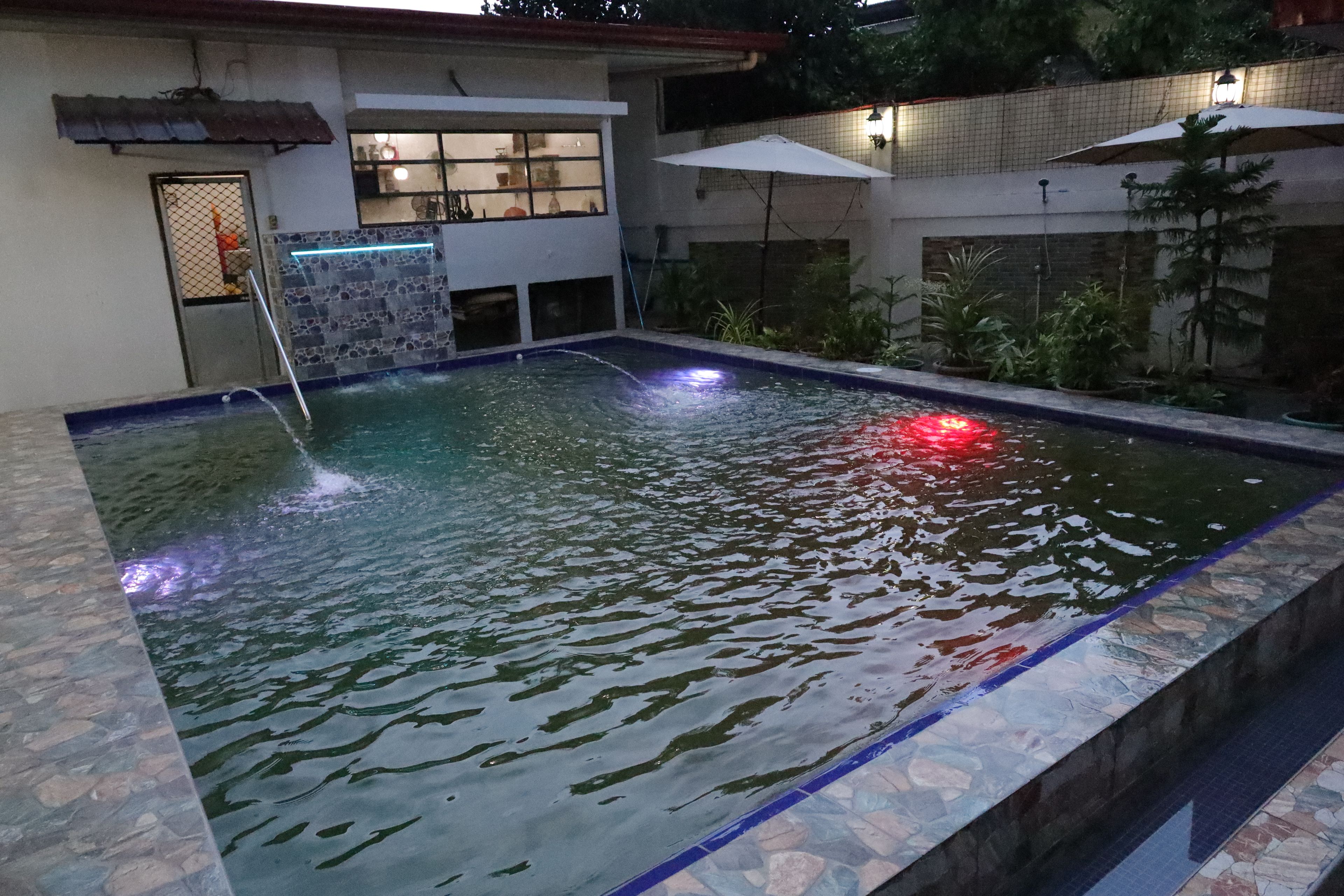 Una piscina con fuente acuática, rodeada por un muro de piedra y macetas con plantas.