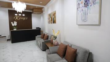 A reception area with a reception desk, a chandelier, a grey sofa, and a painting on the wall.