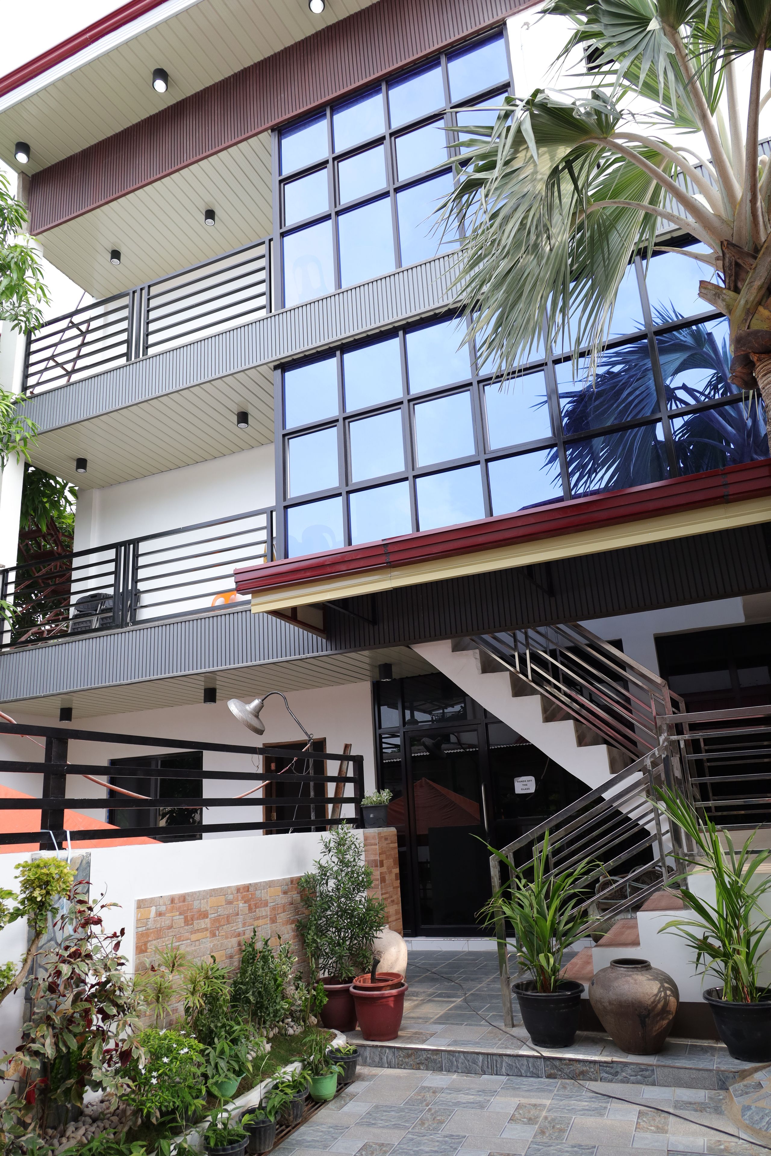 Un edificio de varios niveles con un diseño arquitectónico moderno, que presenta balcones, una escalera y plantas en macetas.