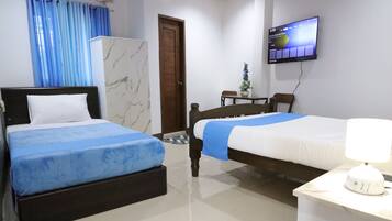 A hotel room with two beds, a TV mounted on the wall, and a small table with a lamp.