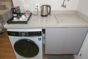 A compact kitchenette with a washing machine, a kettle, and a coffee maker. - Premium studio near Faria Lima (São Paulo)