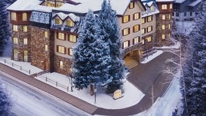Ein mehrstöckiges Hotel mit schneebedecktem Dach und einem großen Weihnachtsbaum davor.