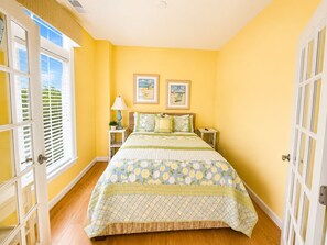 A bedroom with a bed, a nightstand, a lamp, and two framed pictures on the wall. - Sunset Island 2 Shore Point Drive (Ocean City)