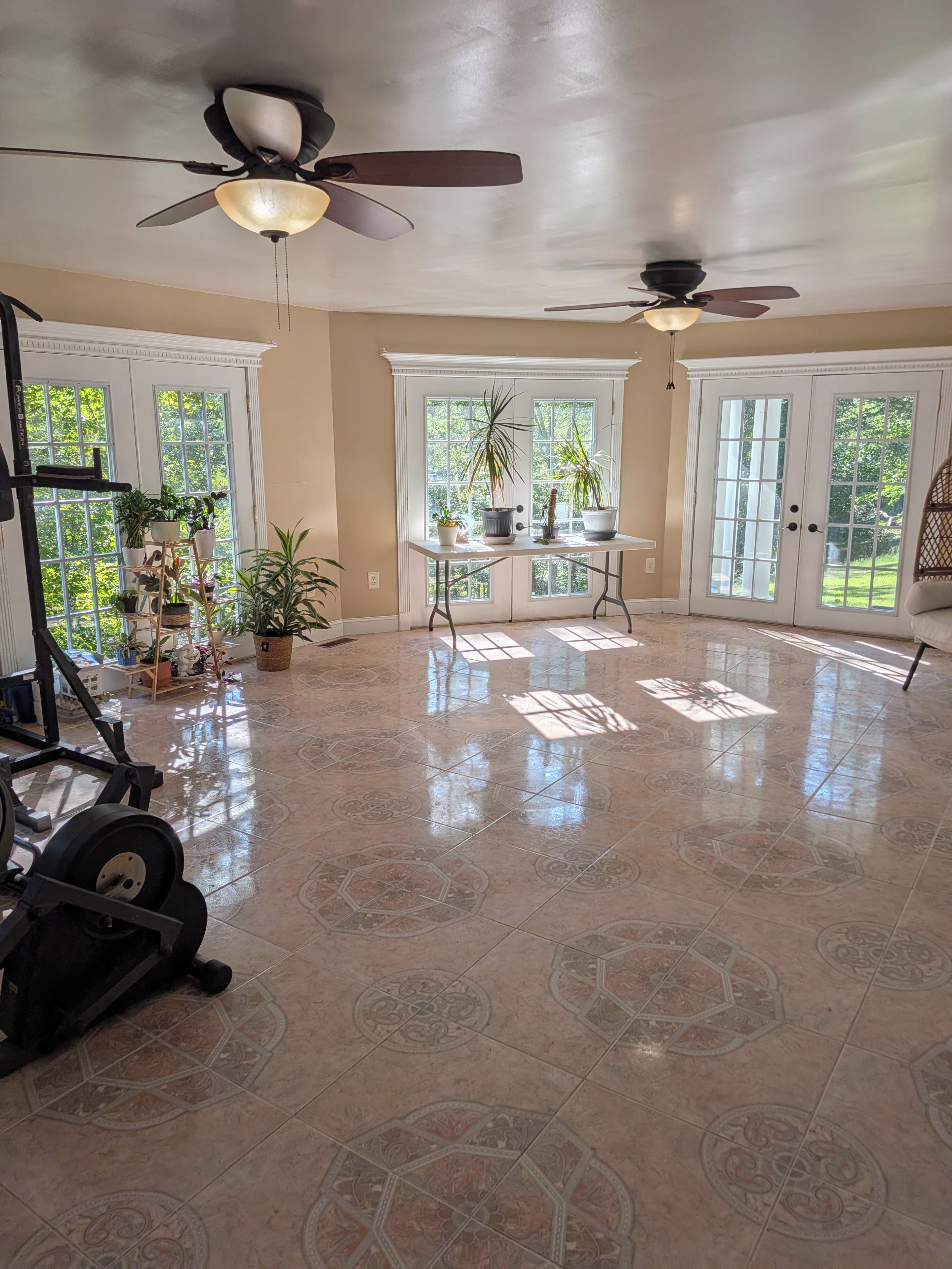 A spacious room with a workout area, a ceiling fan, and a large window with a view of greenery.