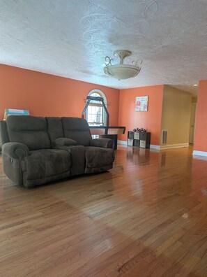A spacious living room with hardwood flooring, a large sofa, a treadmill, and a window with a view.