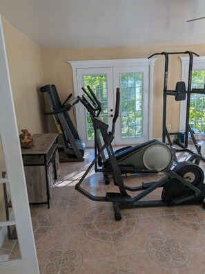 A home gym with exercise equipment, a patterned floor, and a door leading to a balcony with a view of trees.