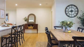 Un coin repas avec une table en bois, des chaises noires, un miroir et une horloge murale.