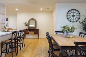A dining area with a wooden table, black chairs, a mirror, and a wall clock.