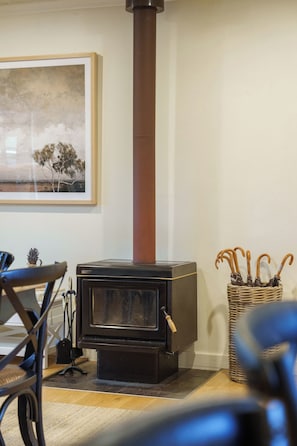 A wood-burning stove with a chimney, a framed picture on the wall, and a wicker basket with umbrellas.