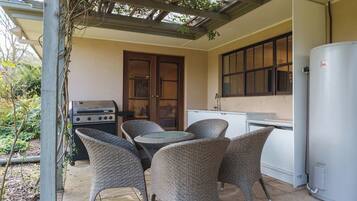 An outdoor patio with wicker chairs, a grill, and a water heater.