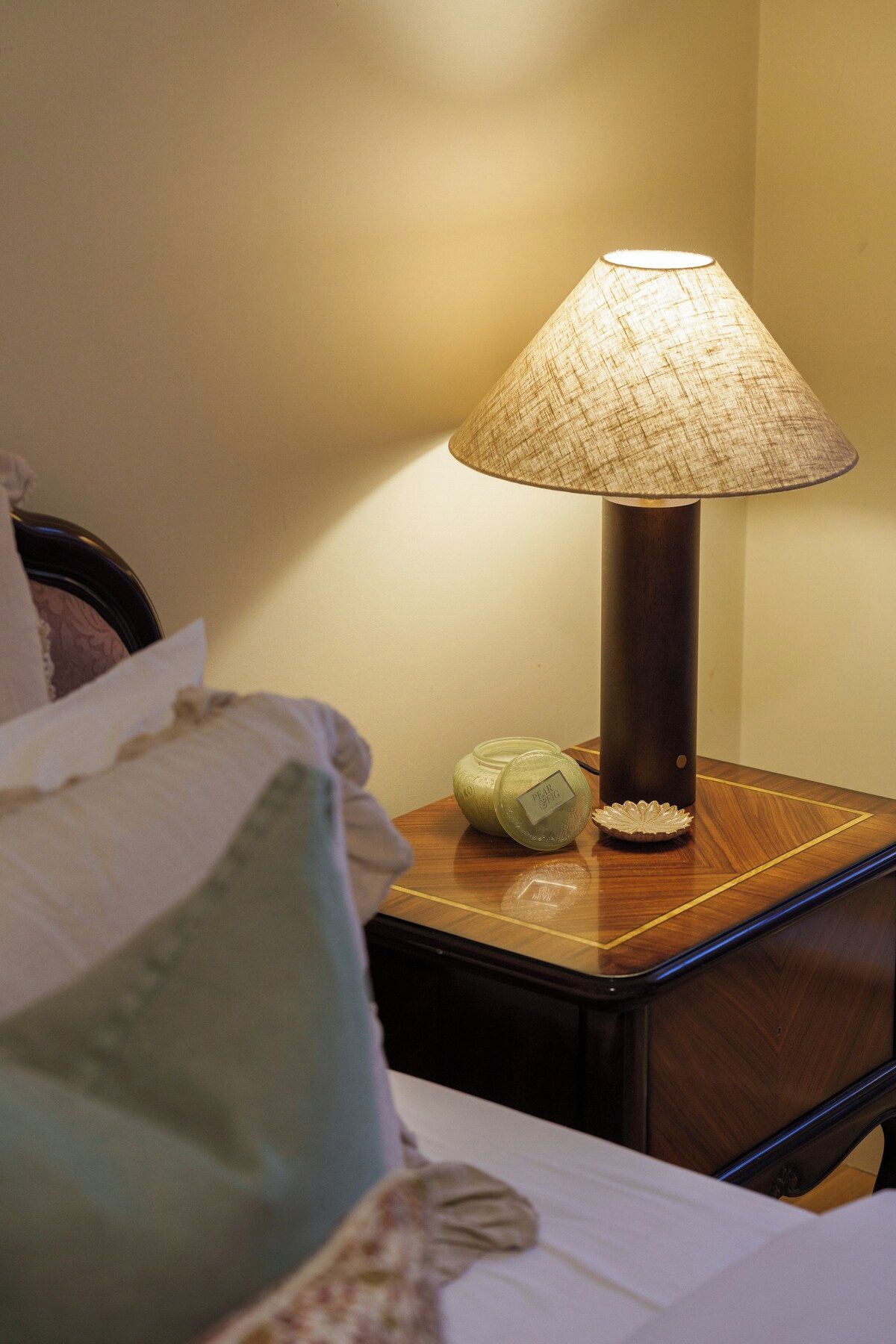 A bedside table with a lamp, a decorative glass jar, and a pillow.