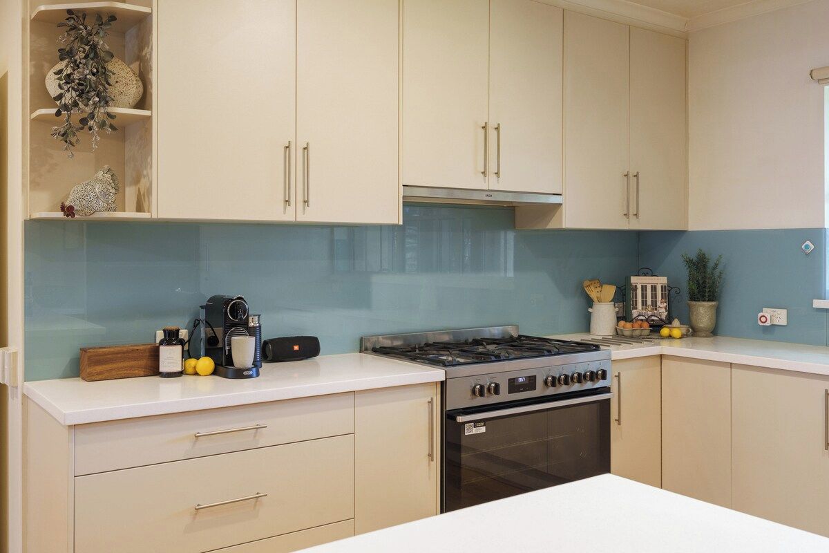 A kitchen with light-colored cabinets, a stove, oven, and a countertop with a coffee maker and lemons.