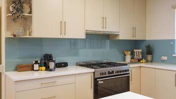 A kitchen with light-colored cabinets, a stove, oven, and a countertop with a coffee maker and lemons.