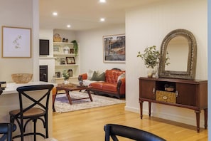 A living room with a red sofa, a wooden coffee table, a dark wooden side table with a mirror, and a white wall with framed artwork.