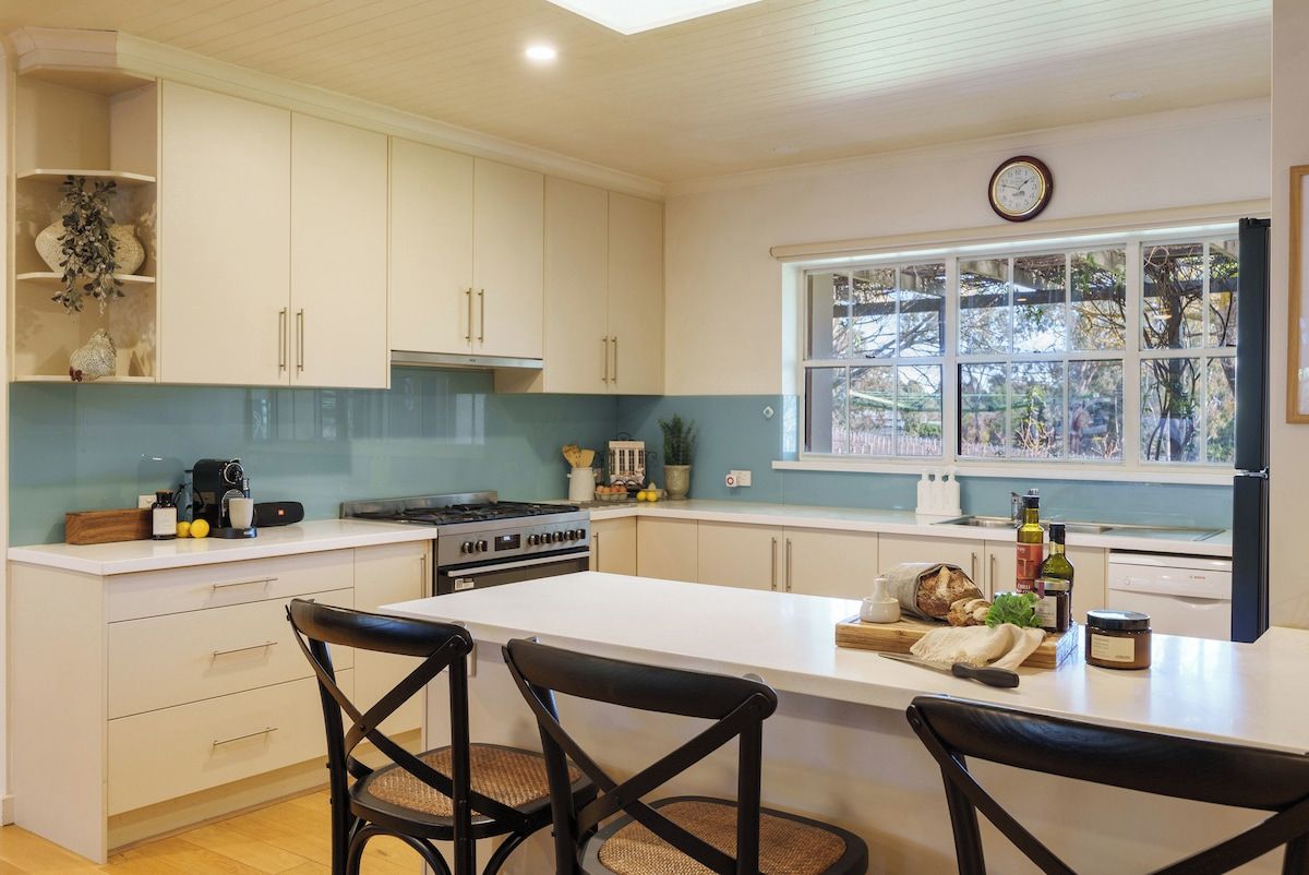 A modern kitchen with white cabinets, a central island, and a window with a view of trees.