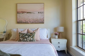 A bedroom with a bed, pillows, a nightstand, a lamp, and a painting on the wall.