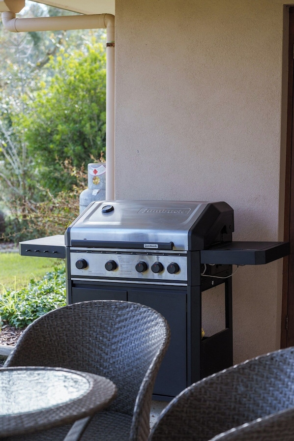 An outdoor grill area with a built-in gas stove, a side table, and wicker chairs.