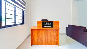 Un comptoir d’accueil avec une pancarte indiquant qu’il s’agit d’un point de collecte desservi par l’entreprise, une fenêtre avec des stores et un canapé de couleur sombre.