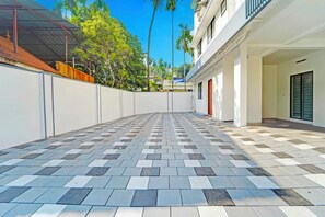 A courtyard with a patterned tile floor, a white wall, and a covered area with a metal roof. - Collection O Kalamassery (Kanayannur)
