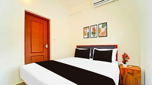Une chambre d’hôtel avec un lit, une table de chevet en bois, un climatiseur fixé au mur et une porte.