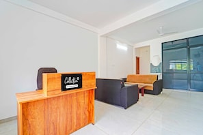 A reception area with a wooden desk, a black sign, a grey sofa, and a glass partition. - Collection O Kalamassery (Kanayannur)