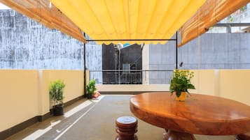 An outdoor patio with a round wooden table, potted plants, and a yellow canopy.