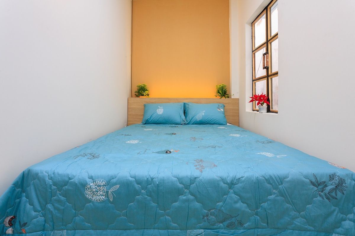 A bedroom with a bed, a window with a view, and a wall with a light fixture.