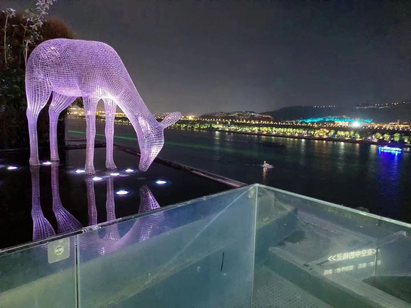 A nighttime view of a waterfront property with a glass railing overlooking a body of water.