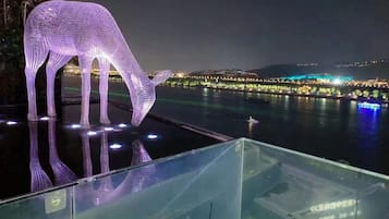 A nighttime view of a waterfront property with a glass railing overlooking a body of water.