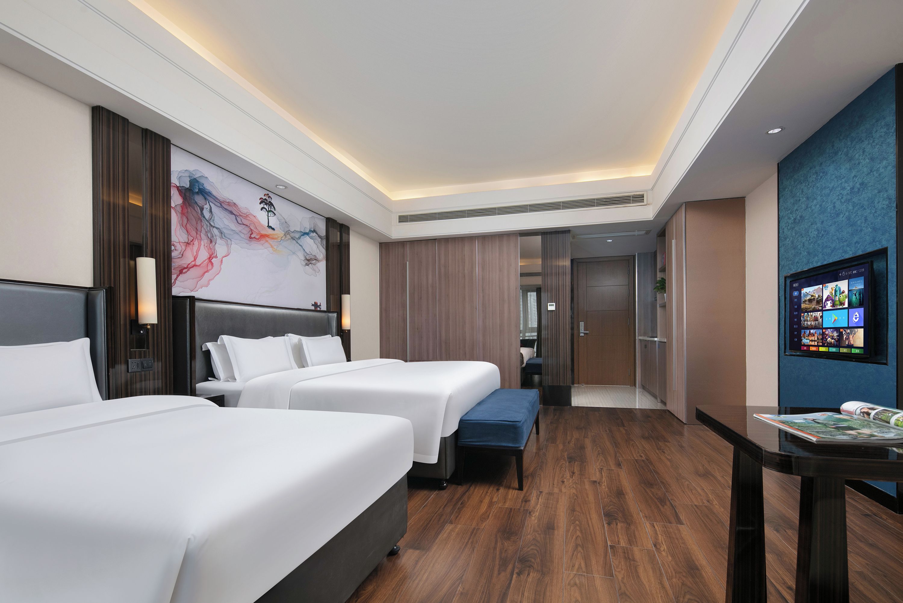 Habitación de hotel con dos camas, un escritorio, un televisor y un cuadro abstracto grande en la pared.