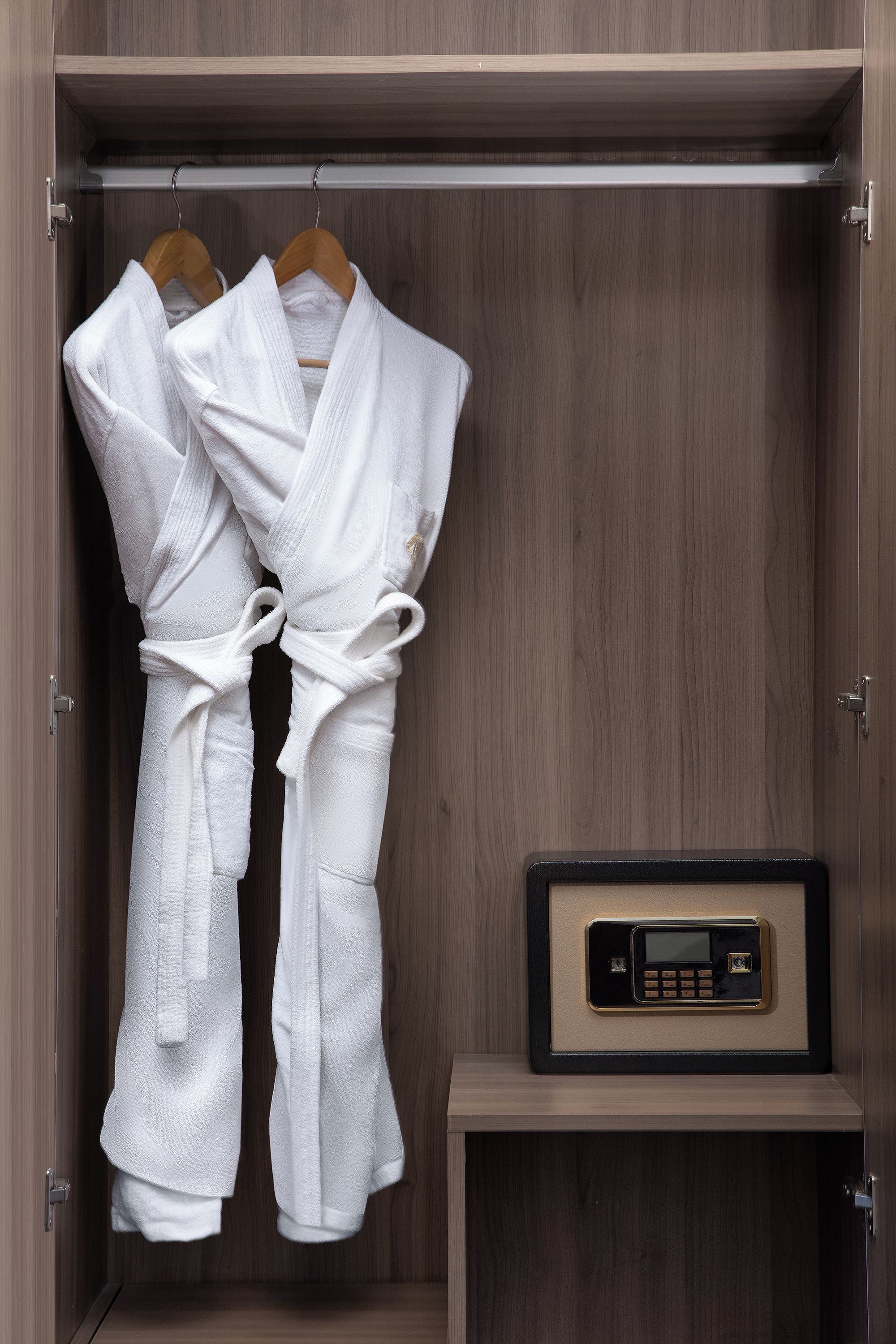A wooden wardrobe with two white robes hanging on hangers and a black electronic device on a shelf.