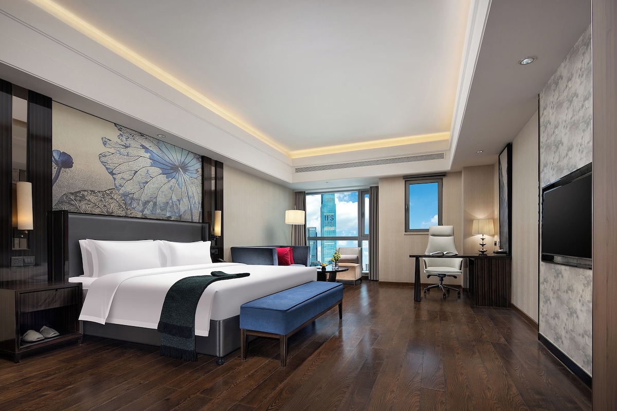 Habitación de hotel con una cama grande, un escritorio, una silla, un televisor y vistas de la ciudad.