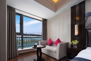 Habitación de hotel con sofá, una mesita, lámpara y vista panorámica de la ciudad a través de un ventanal.