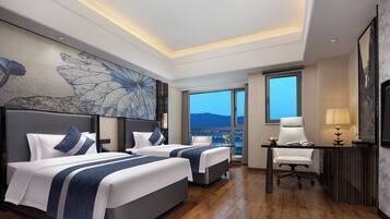 A hotel room with two beds, a desk, a chair, and a large window offering a city view.