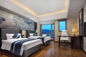 Habitación de hotel con dos camas, un escritorio, una silla y un amplio ventanal con vistas a la ciudad.