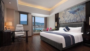 Ein Hotelzimmer mit Bett, Schreibtisch, Stuhl, großem Fenster und Blick auf die Landschaft.